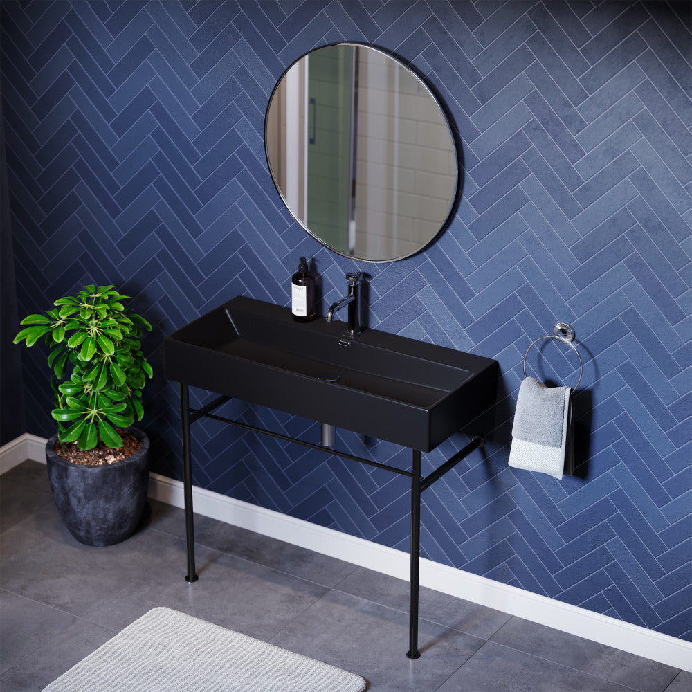 40-inch matte black ceramic console sink with slim black metal legs and round mirror on blue herringbone wall.