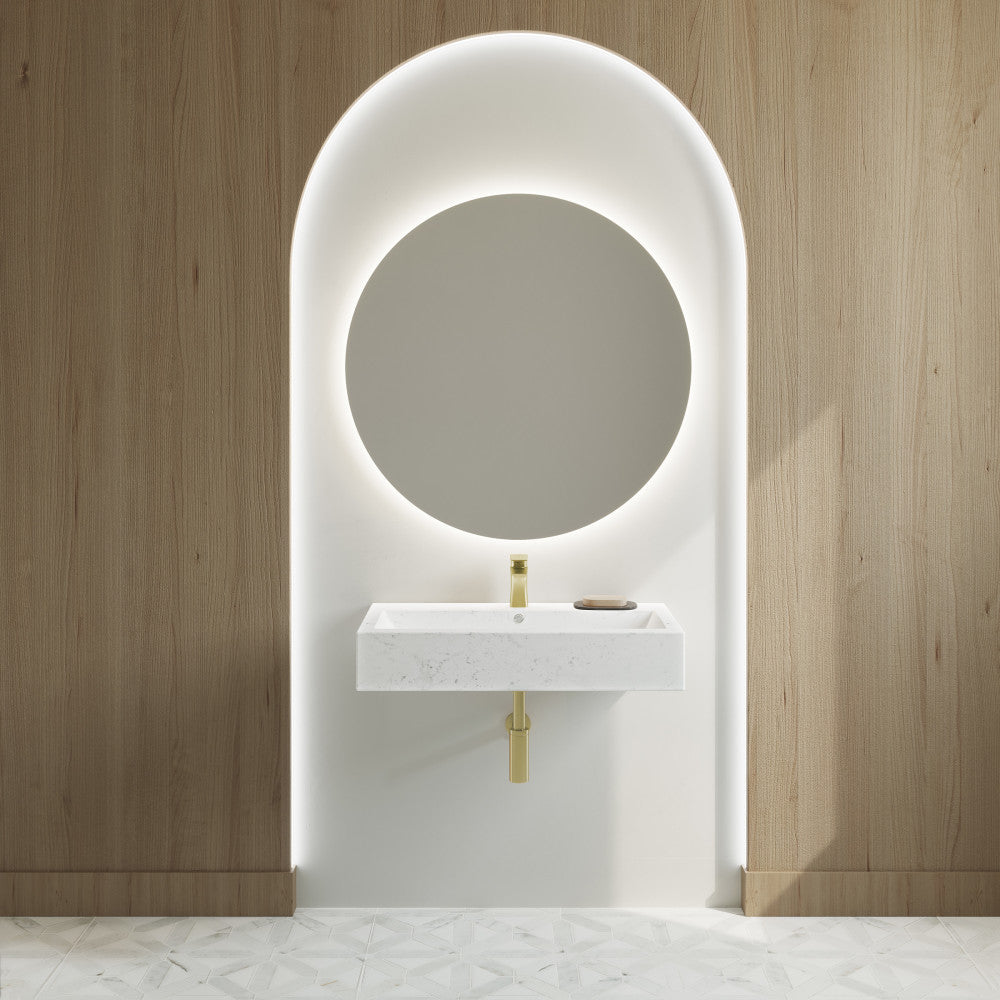 Wide rectangle wall-hung bathroom sink in static white marble with gold faucet, mounted on white niche with wood walls.