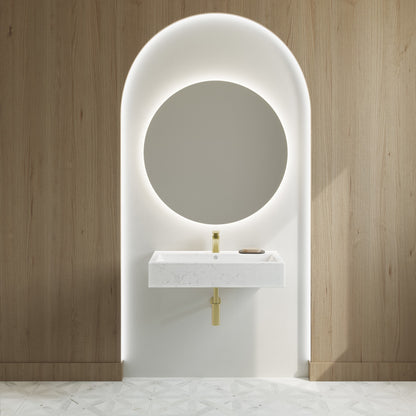 Wide rectangle wall-hung bathroom sink in static white marble with gold faucet, mounted on white niche with wood walls.