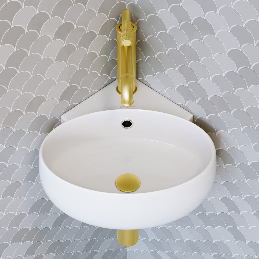 Round wall-hung bathroom sink in white with gold drain cover and gold faucet against gray scale tile wall.