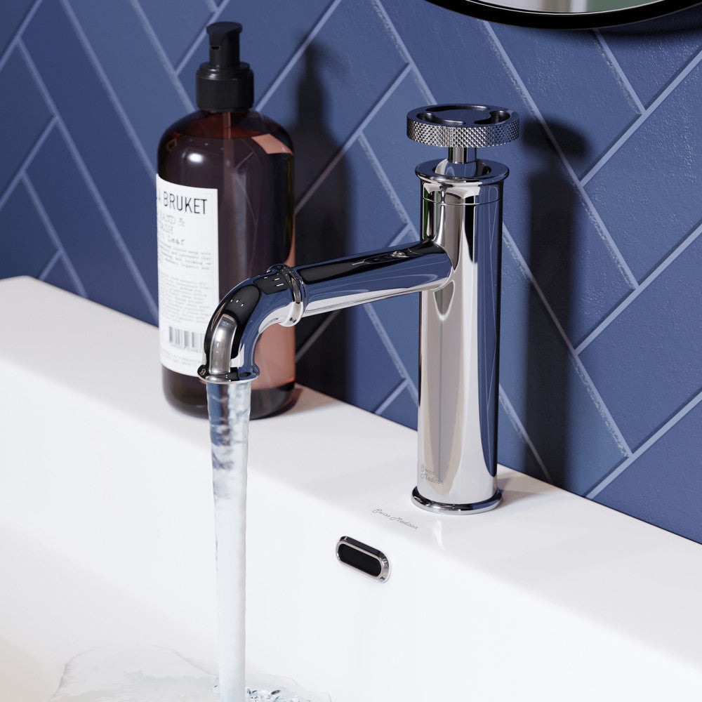 Single-handle bathroom faucet in chrome with wheel handle, water flowing from spout on white sink top.