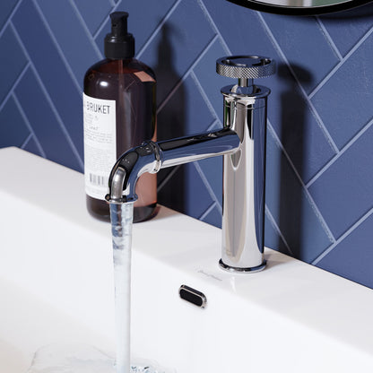 Single-handle bathroom faucet in chrome with wheel handle, water flowing from spout on white sink top.