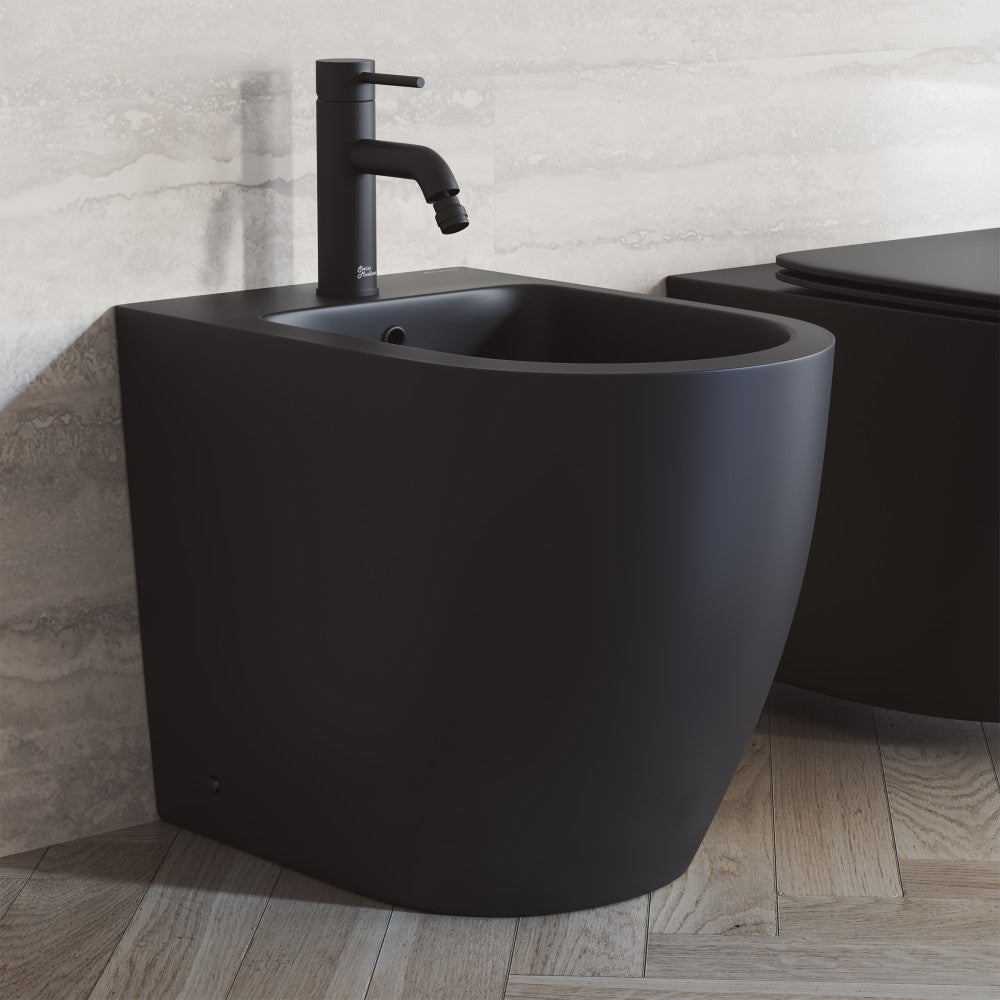 Matte black floor-mount bidet with smooth rounded edges and single-hole faucet on wooden floor.