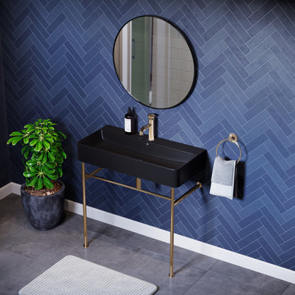 Matte black ceramic console sink with gold legs, rectangular basin, wall-mounted faucet, and round mirror.
