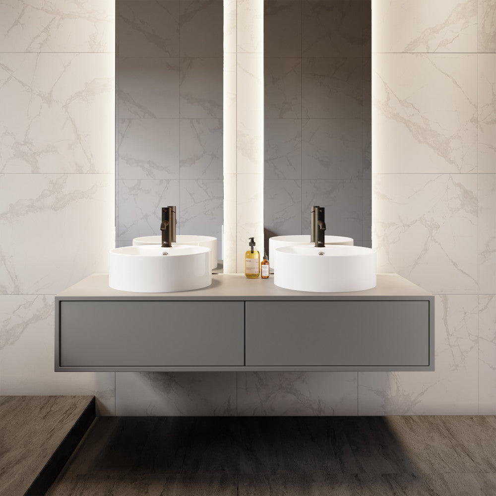 Round white vessel sink with faucet mount on a floating gray vanity against marble wall.