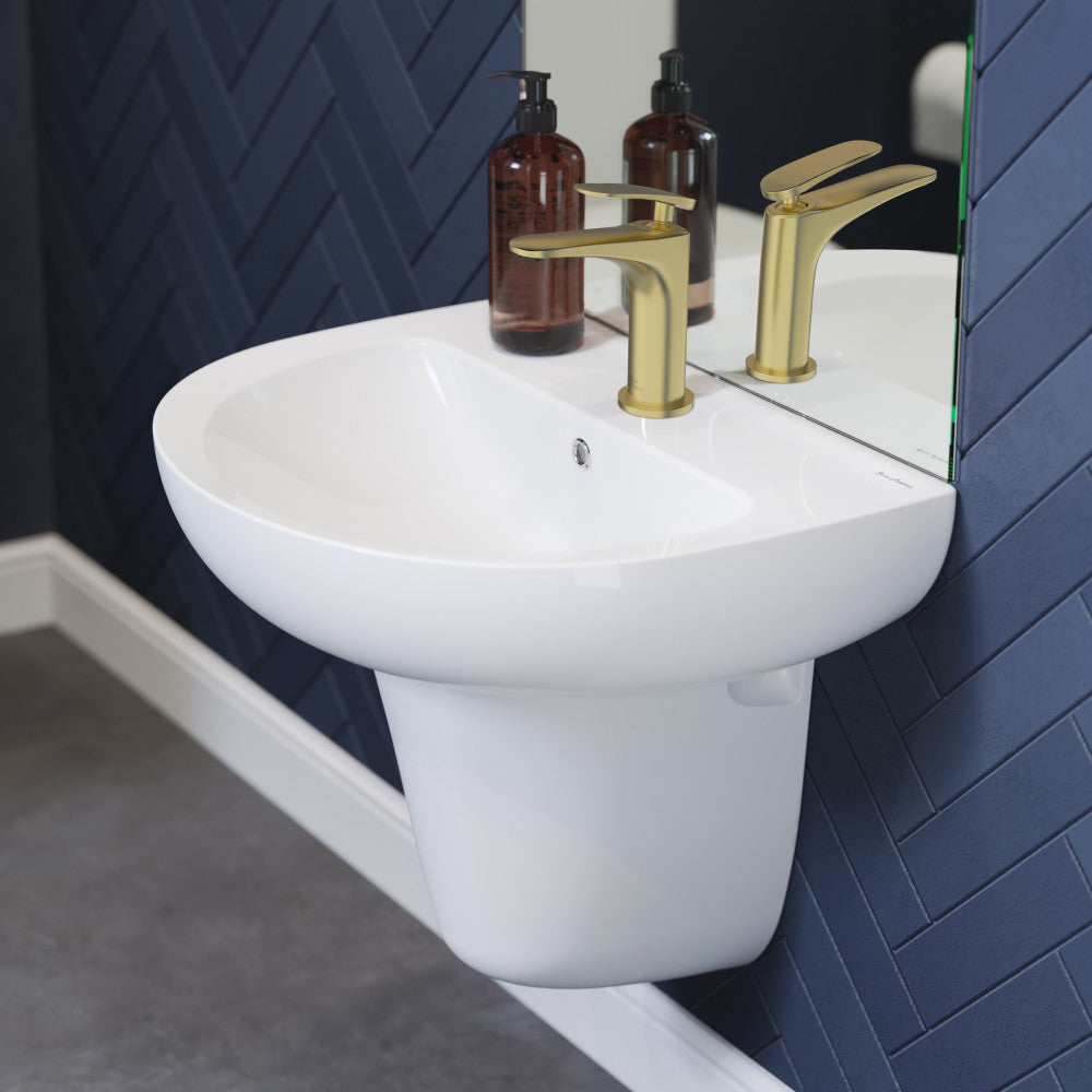 White ceramic wall-mount sink with gold single-handle faucet against navy blue wall.