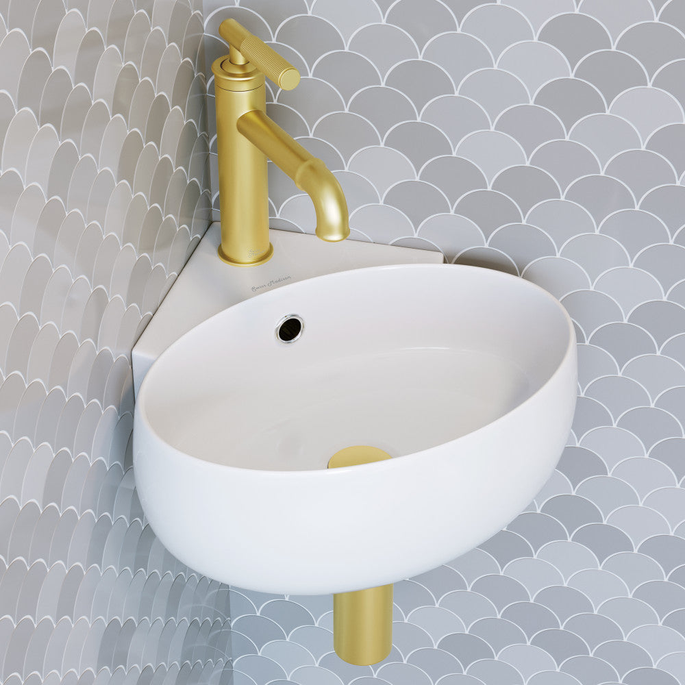 Small white wall-hung corner sink with single hole and gold matte faucet against textured gray tile wall.