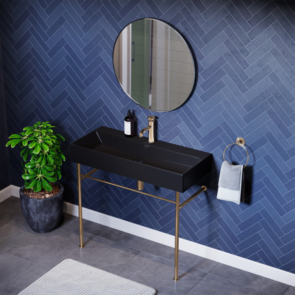 Matte black ceramic console sink with gold legs and round wall mirror in modern bathroom setting.